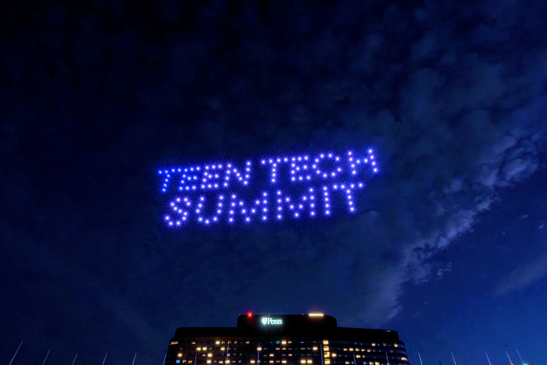 Multicolored drone lights forming an abstract emblem above a Penn campus building at night