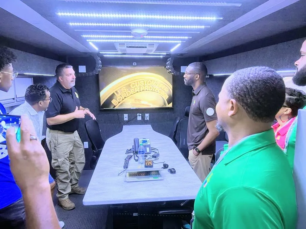 People gathered around a conference table inside a mobile command vehicle with a U.S. Customs and Border Protection graphic on the screen