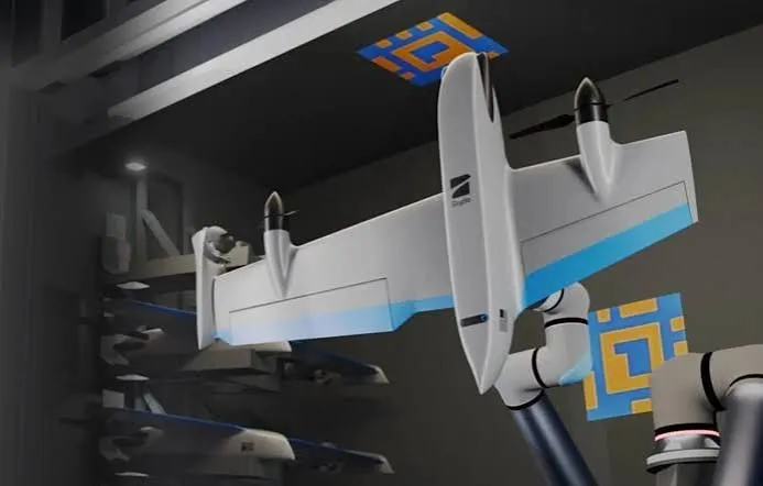 Large white tail-sitter drone being handled by a white robot arm inside a hangar